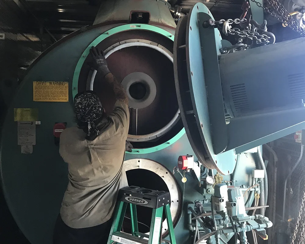 A worker performs maintenance on an industrial boiler