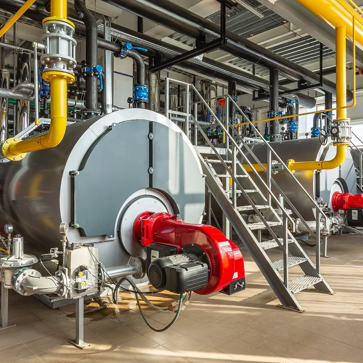 A wide-angle view of a large industrial boiler with a bright red burner unit and surrounding metal stairways, pipes, and machinery.