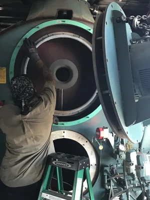 A worker performs maintenance on an industrial boiler